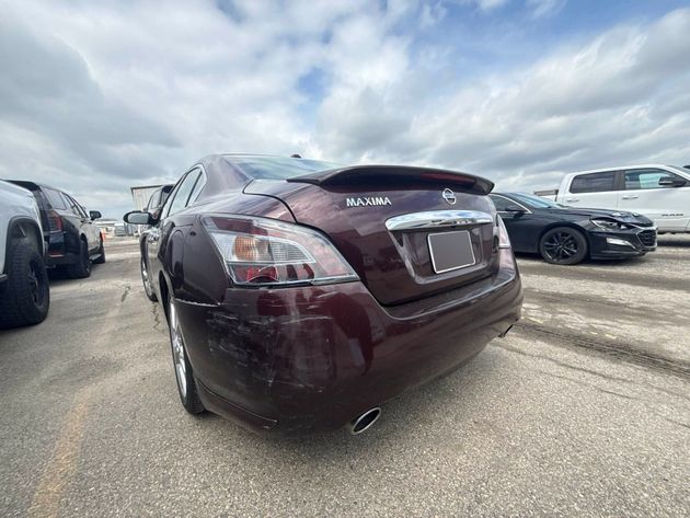 Maroon sedan parked in a car lot, rear view with cloudy sky overhead