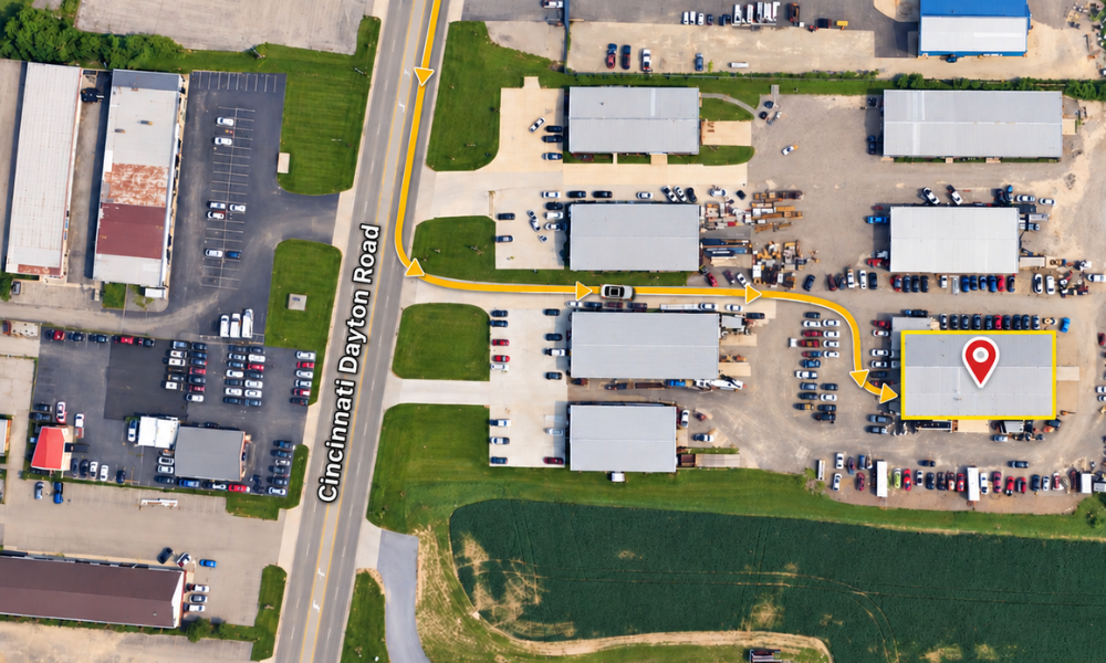 Aerial view of an industrial park with warehouses, parking lots, and a marked route near a road and field