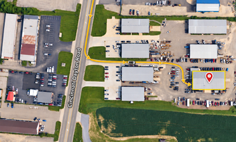 Aerial view of an industrial park with warehouses, parking lots, and a marked route near a road and field