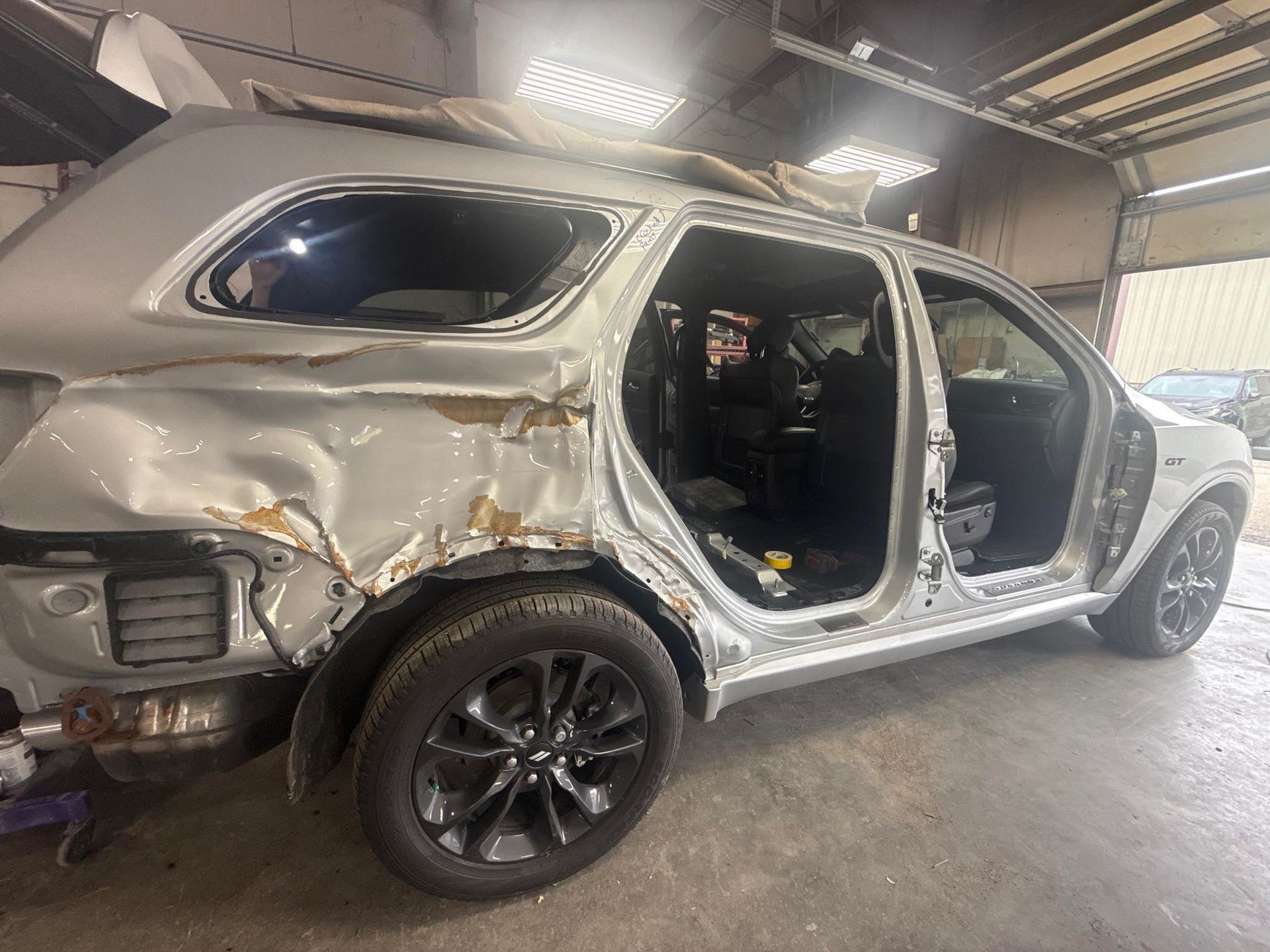 Damaged silver SUV in a garage, with crumpled rear quarter panel and missing doors.