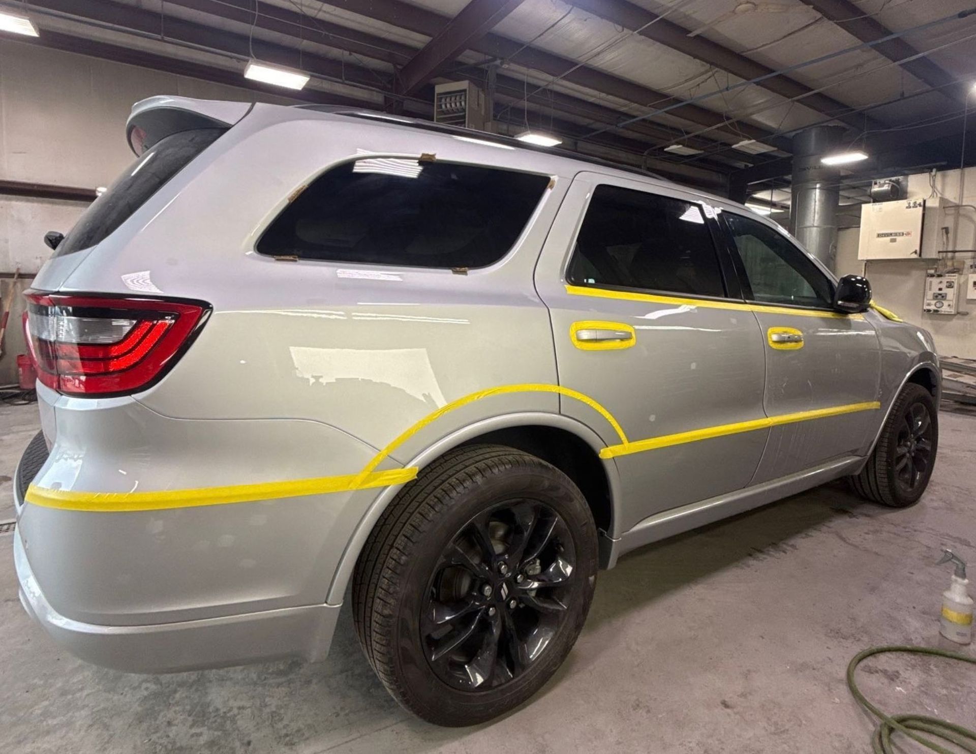 Silver SUV in a workshop, with yellow tape marking areas along the side and rear wheel arch.