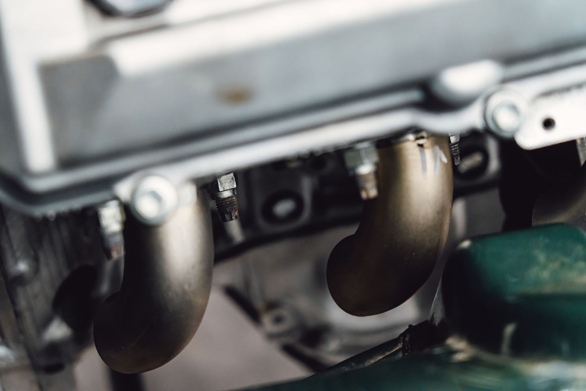 Close-up of a car engine featuring exhaust headers, nuts, and bolts, with a green component in the foreground.