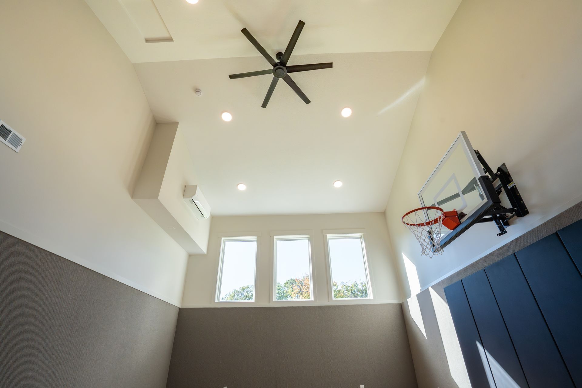 Basketball hoop in a bright indoor gym with high ceiling, windows, and ceiling fan
