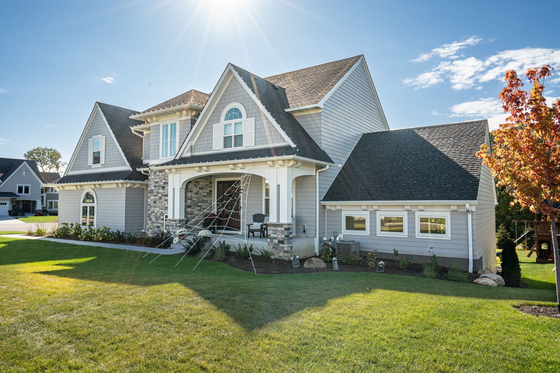 Suburban house with stone facade, gabled roof, and a bright green lawn in sunlight