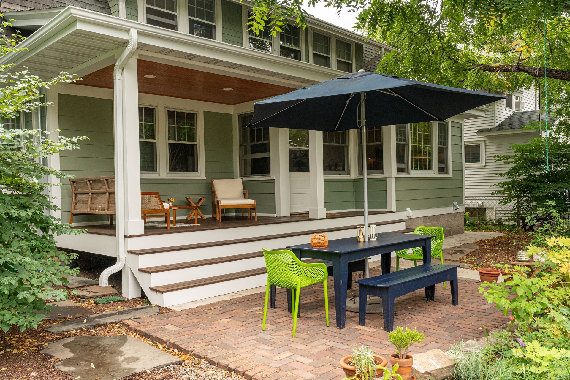 Covered front porch with white rocking chairs, a large black patio umbrella, and bright green and navy outdoor seating.