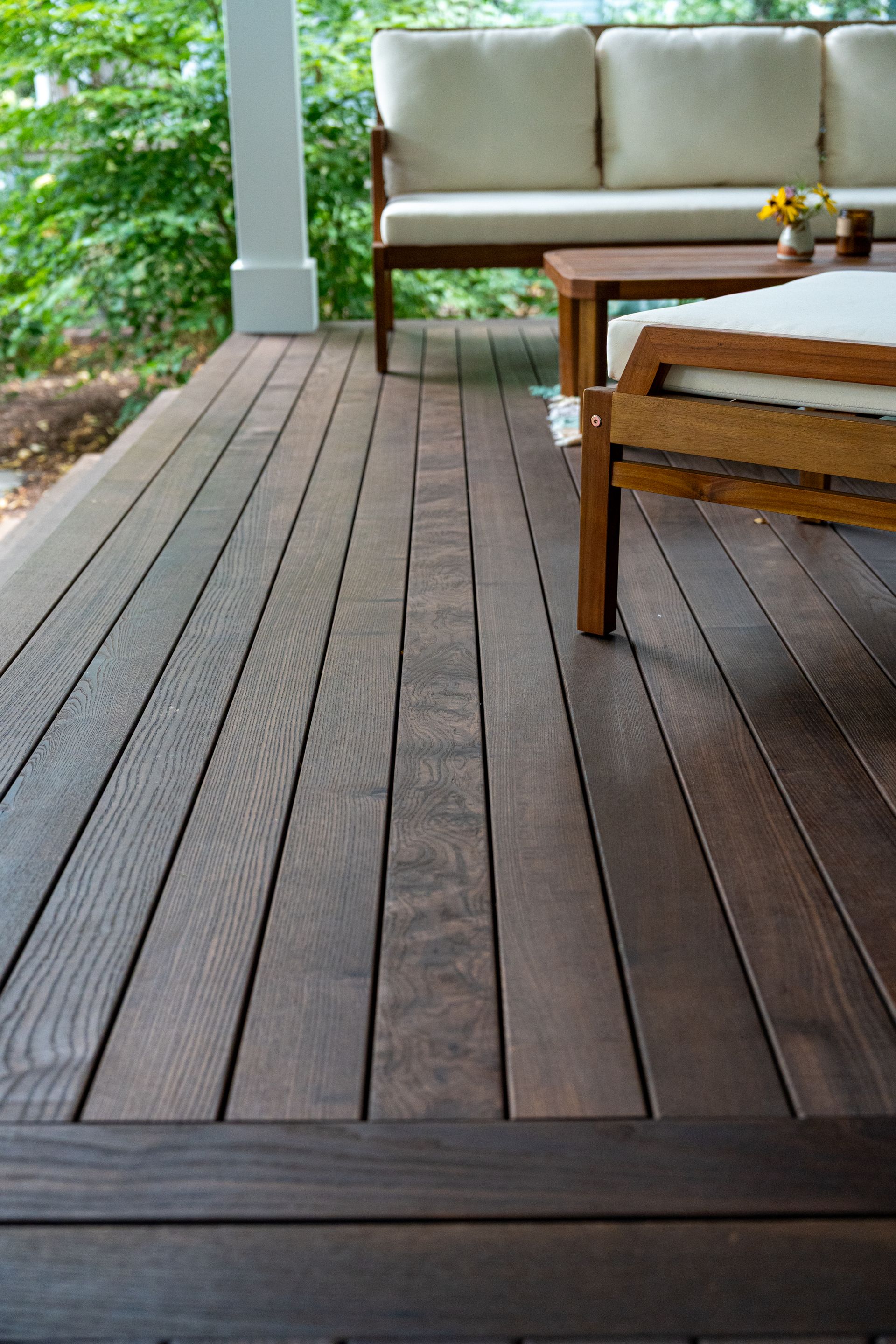Wooden porch deck with beige sofa and wicker chair beside green garden
