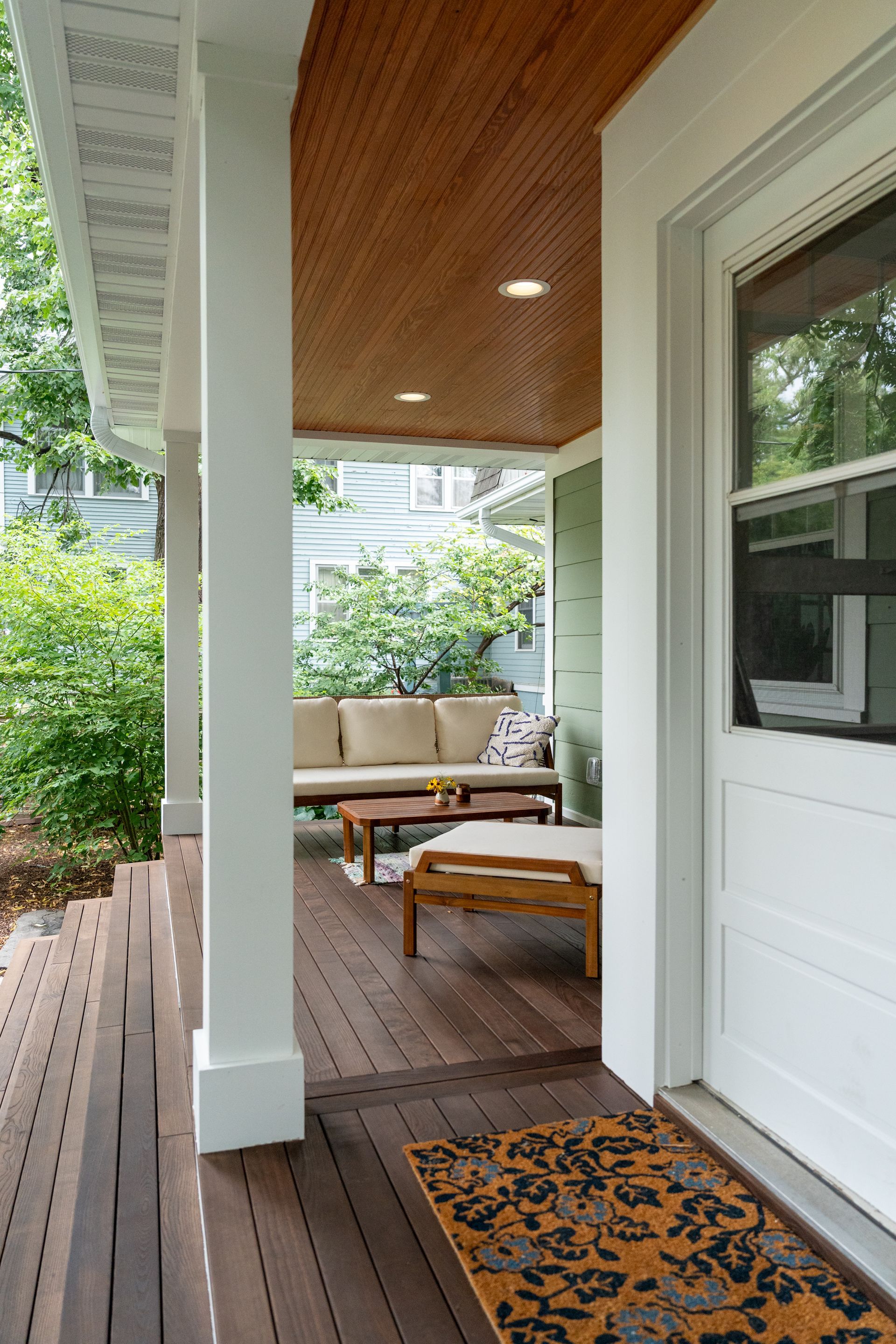Front porch with wood decking, white columns, a bench, and an orange patterned rug.