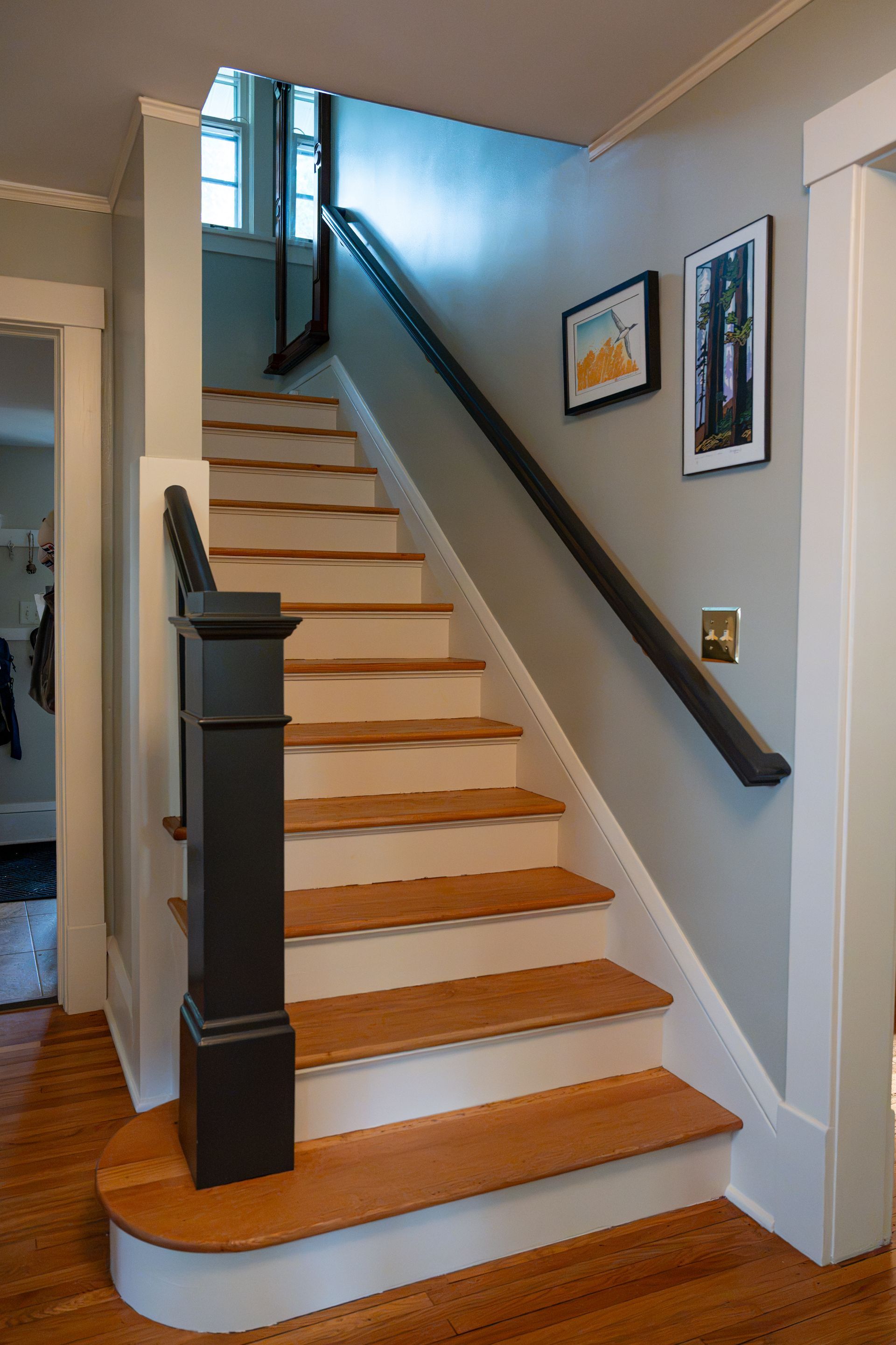 Staircase with wooden steps, white risers, dark handrail, and framed art on light gray walls.