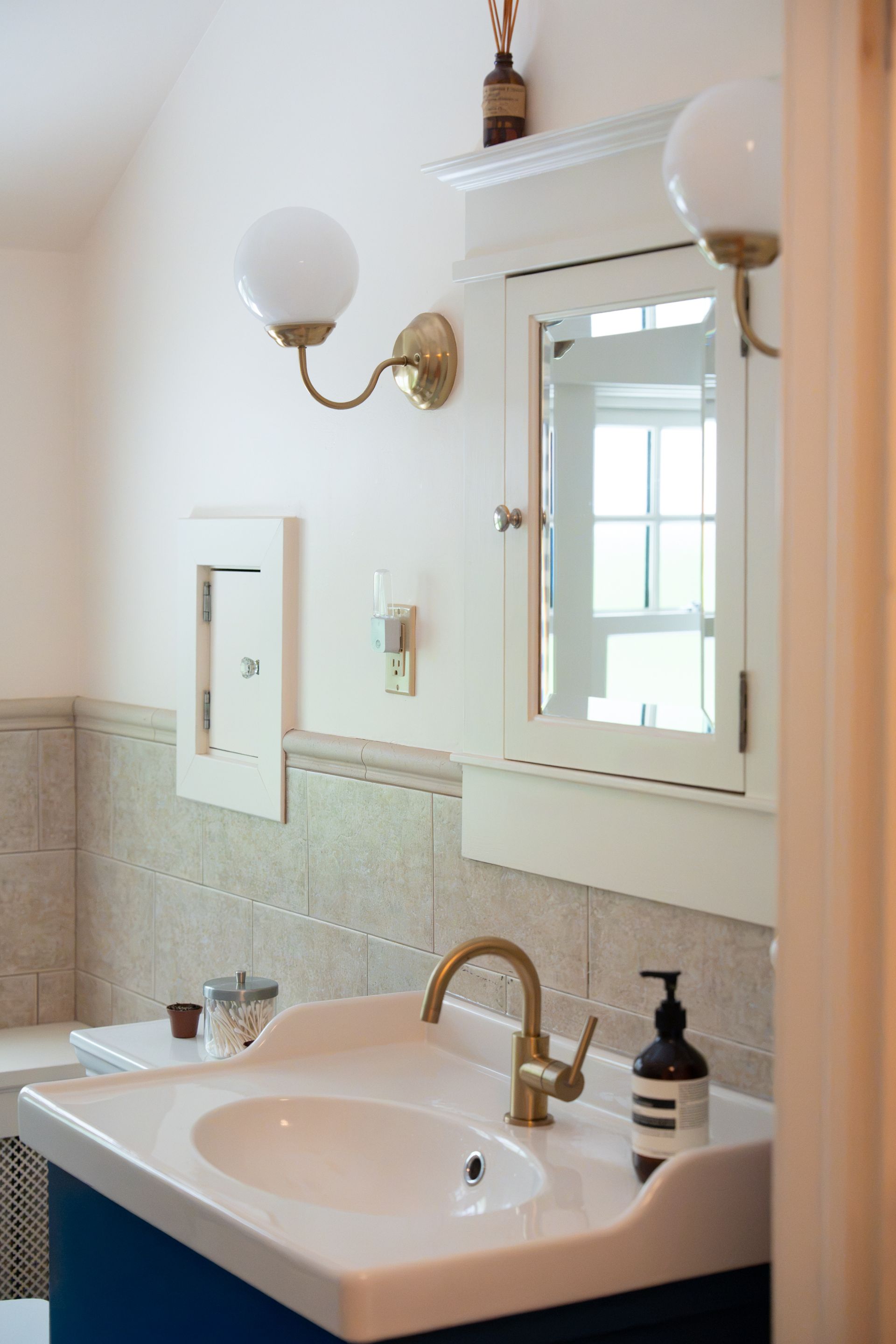 Bright bathroom vanity with mirror, sink, brass faucet, wall sconces, and a soap dispenser