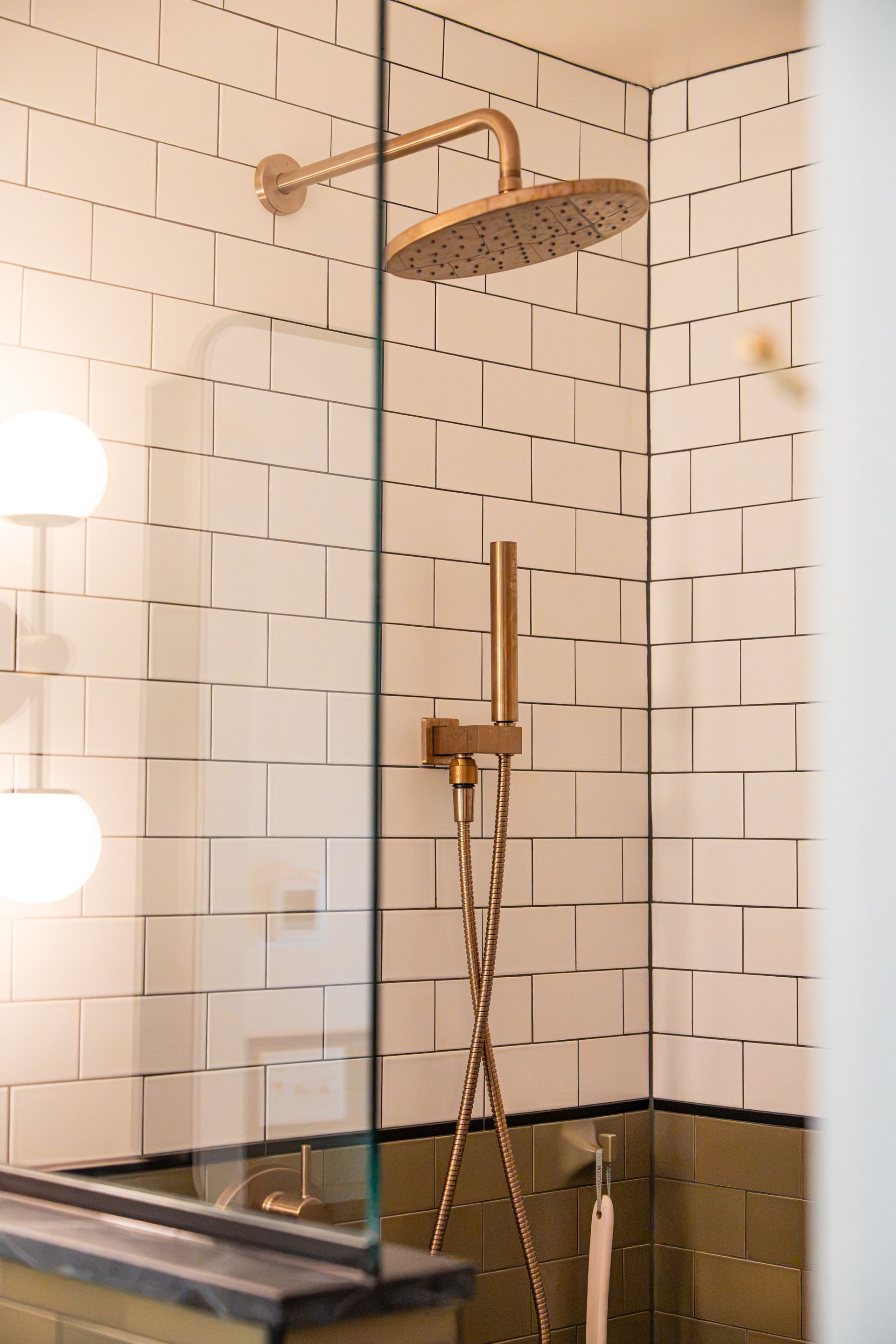 Modern bathroom shower with white subway tiles, brass fixtures, and a handheld showerhead over a bathtub