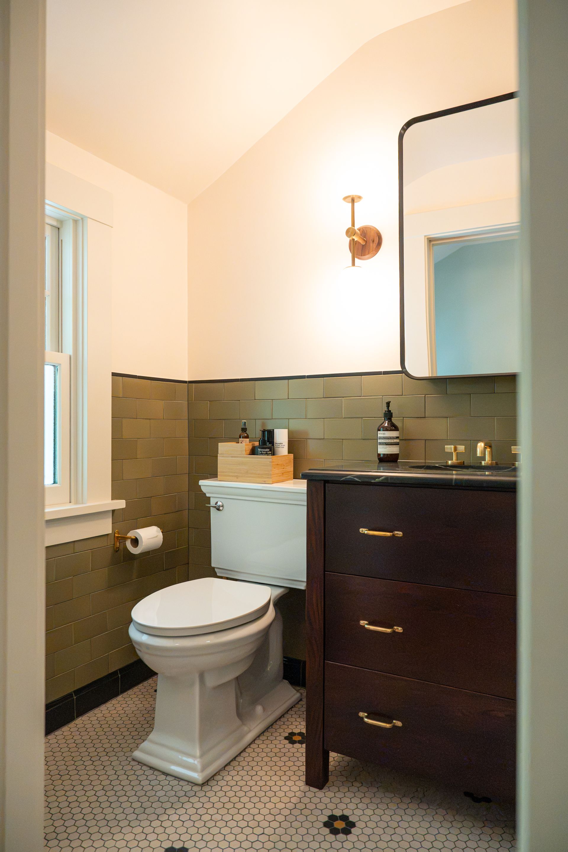 Compact bathroom with toilet, dark vanity, and beige tile walls and floor