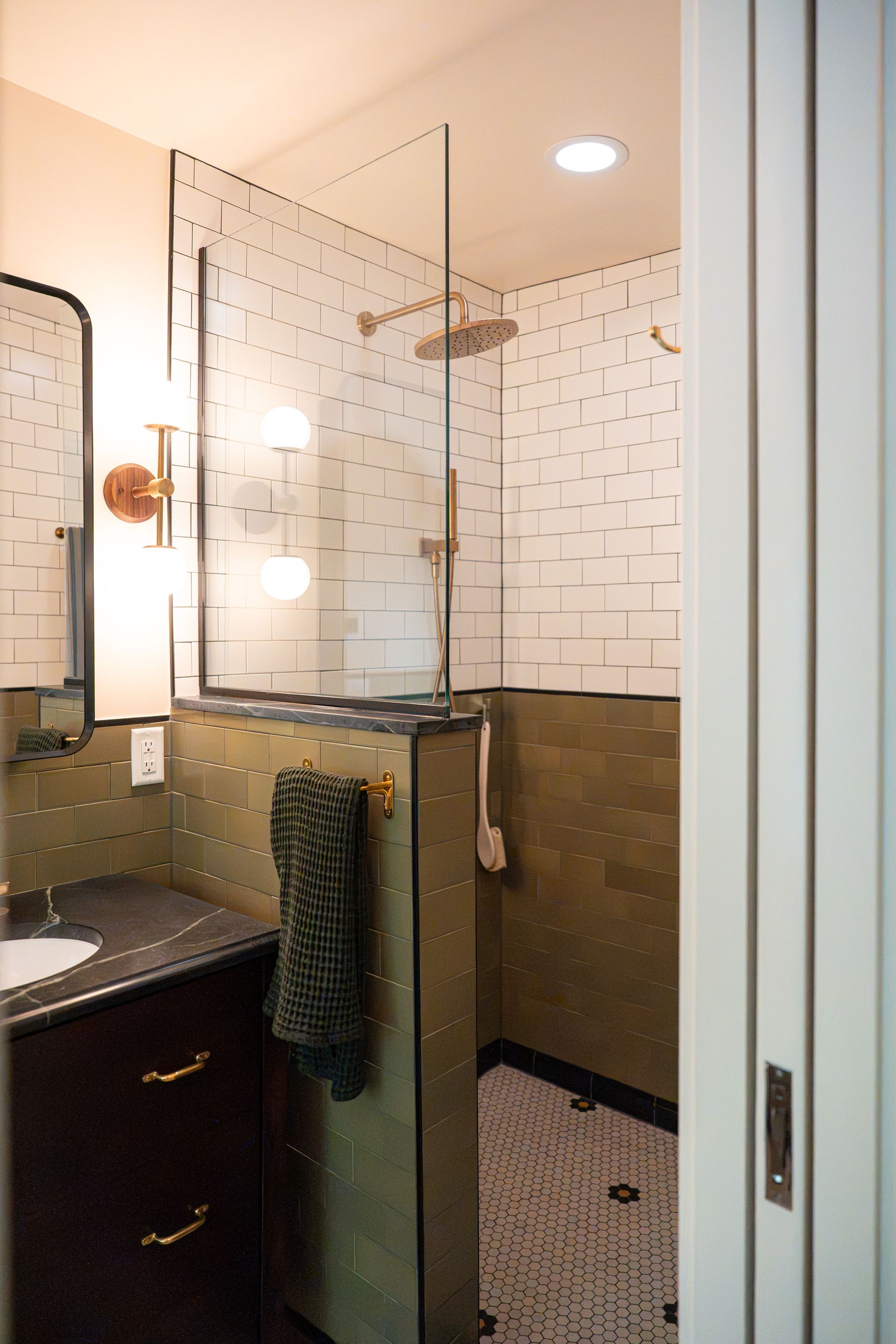 Small bathroom with glass shower, white tiled walls, dark vanity, and towel hanging nearby.