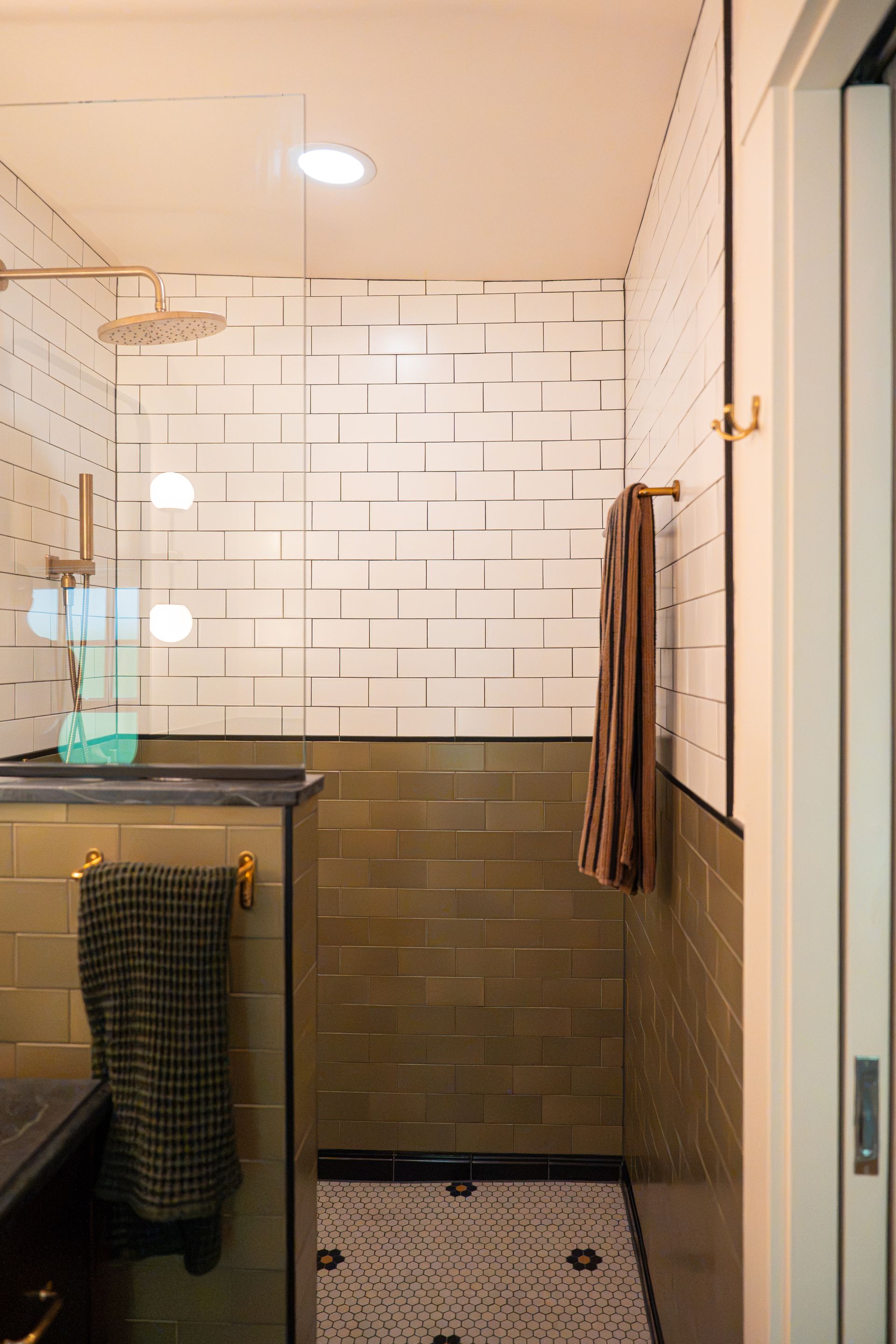 Modern bathroom with glass shower, white tiled walls, and brown tiled lower walls.