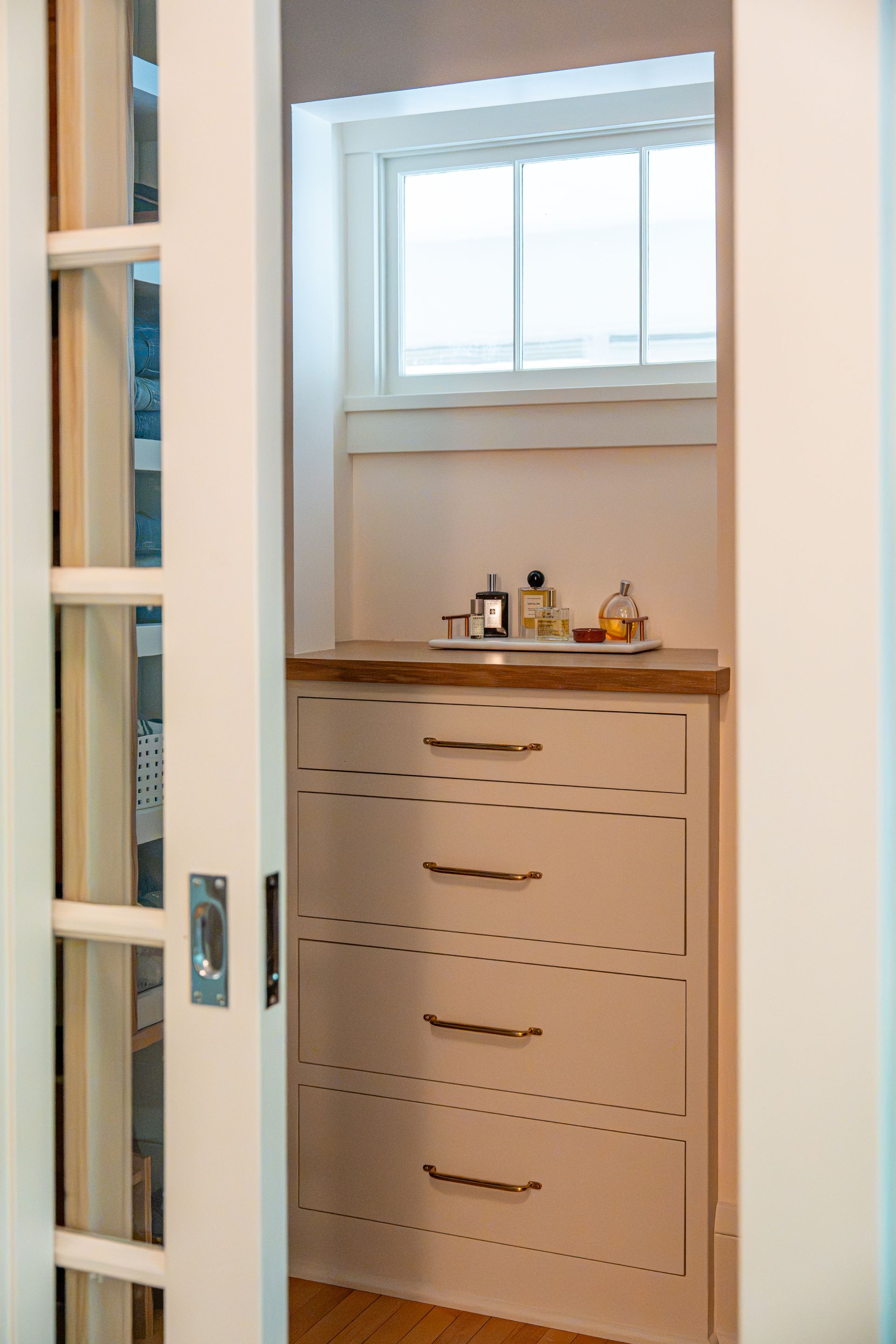 Open closet with white drawers, window above, and toiletries on a wooden counter.