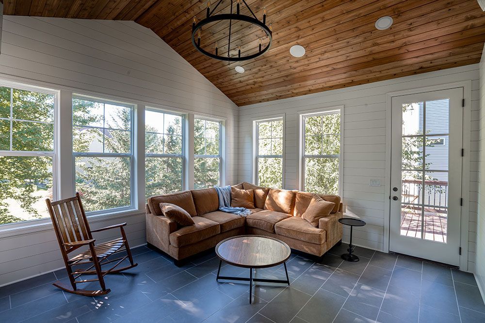 Bright sunroom with tan sectional sofa, rocking chair, round coffee table, and wood ceiling with skylight.