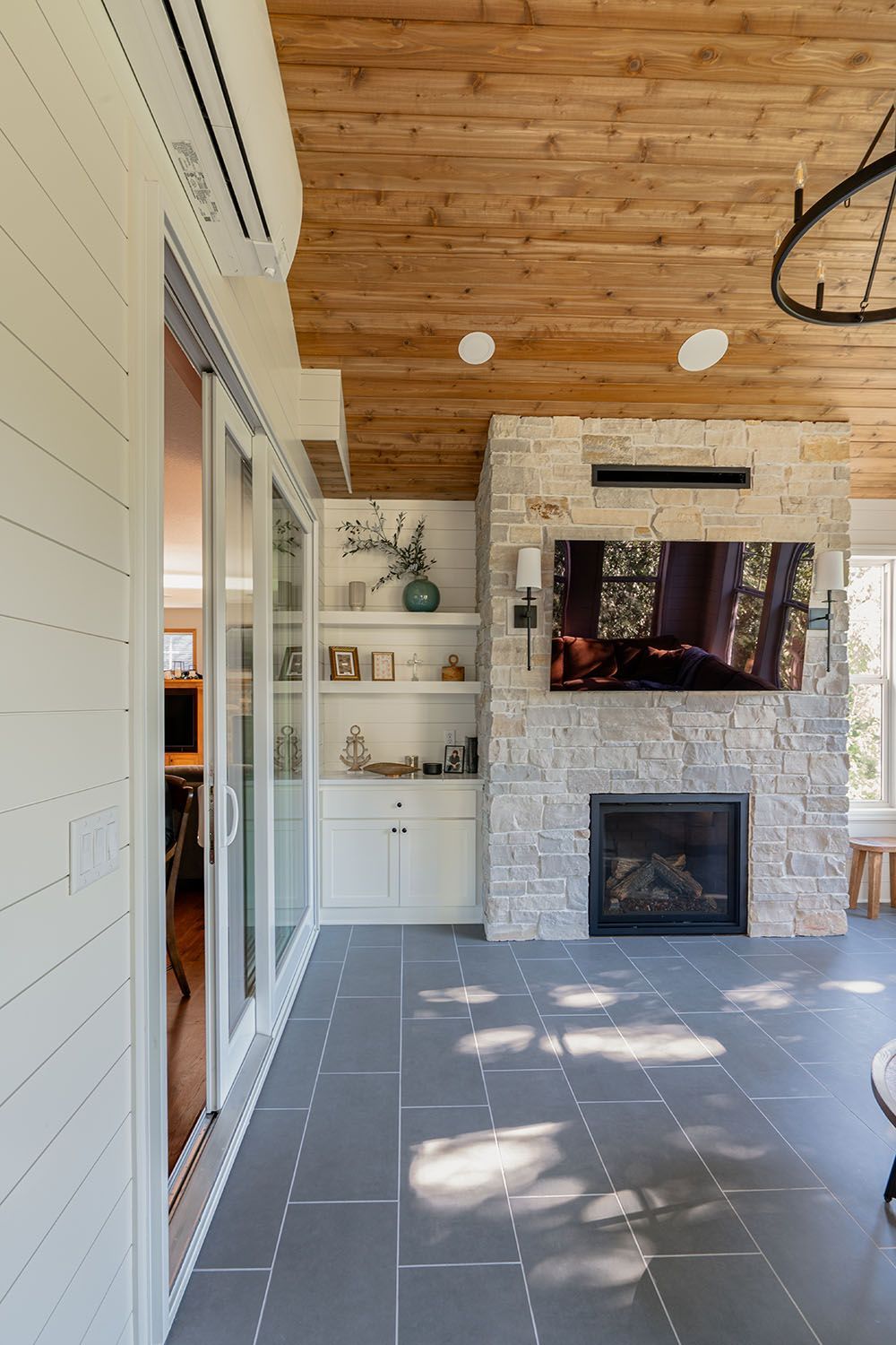 Covered patio with stone fireplace, wooden ceiling, built-in shelves, and gray tile floor.