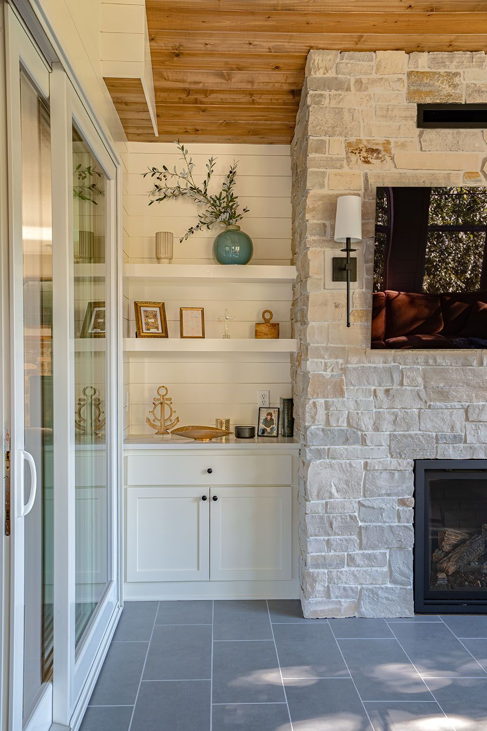 Built-in white shelves beside a stone fireplace on a covered patio with sliding glass doors