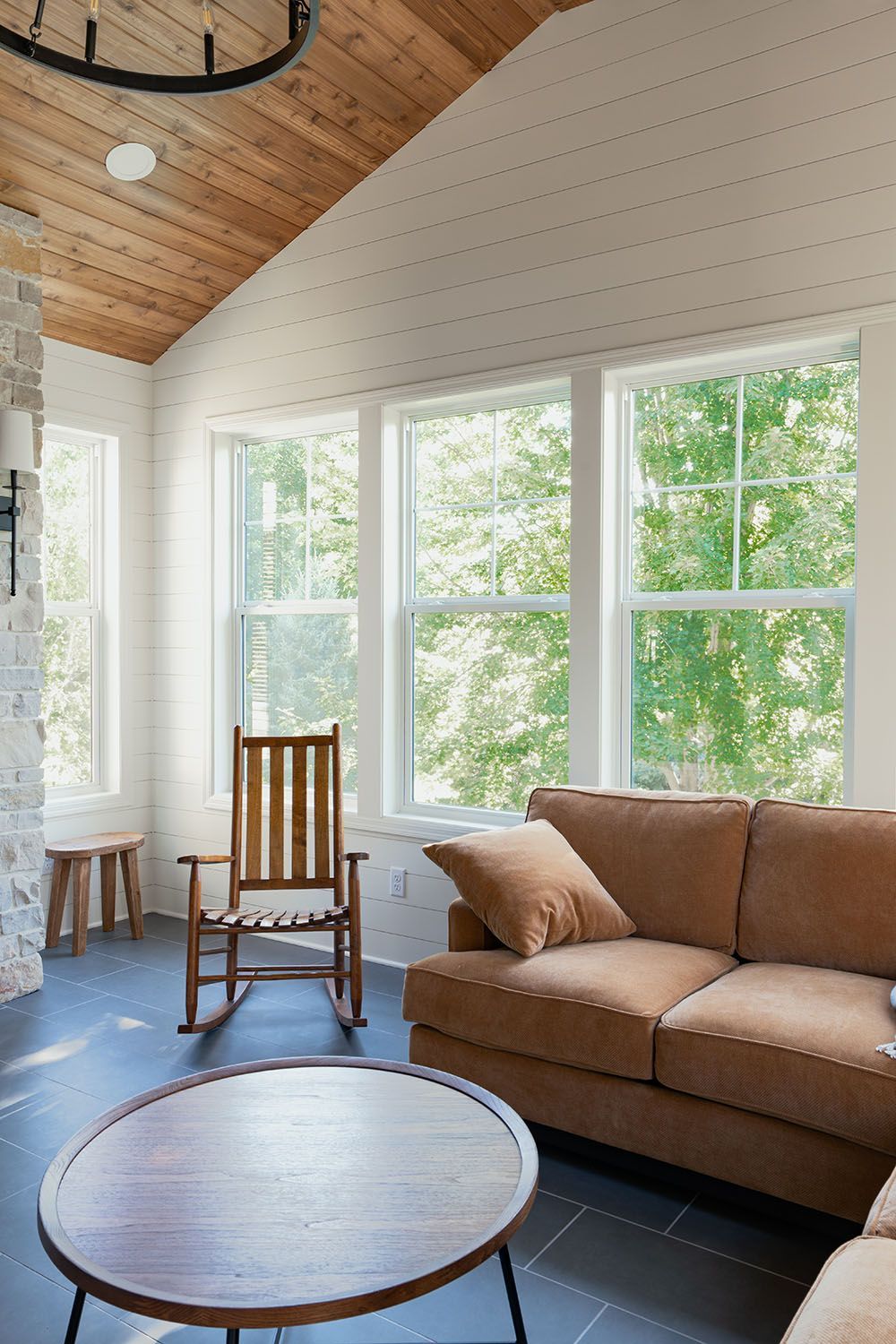 Bright living room with tan sofa, rocking chair, round coffee table, and large windows