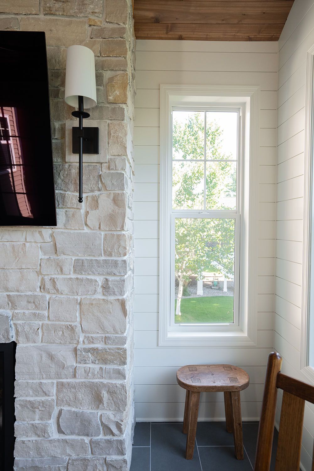 Narrow window in a rustic whitewashed room with stone wall, wall sconce, and a small wooden stool.