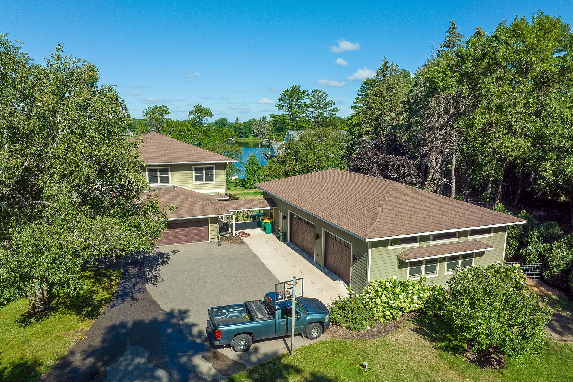 Aerial view of a green house with a brown roof and a blue pickup truck in the driveway. Trees surround the property.