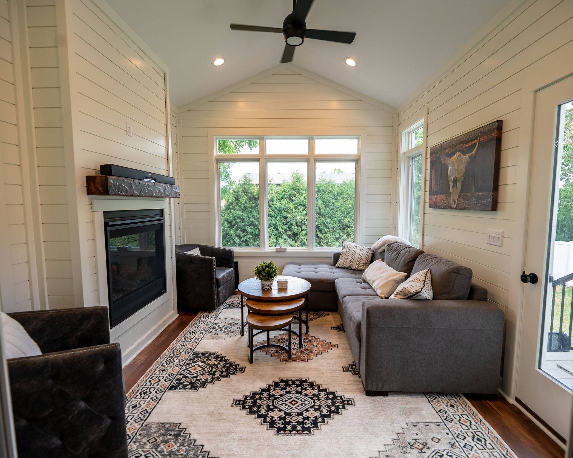 Cozy living room with fireplace, sectional sofa, and large windows overlooking greenery. Neutral color palette.