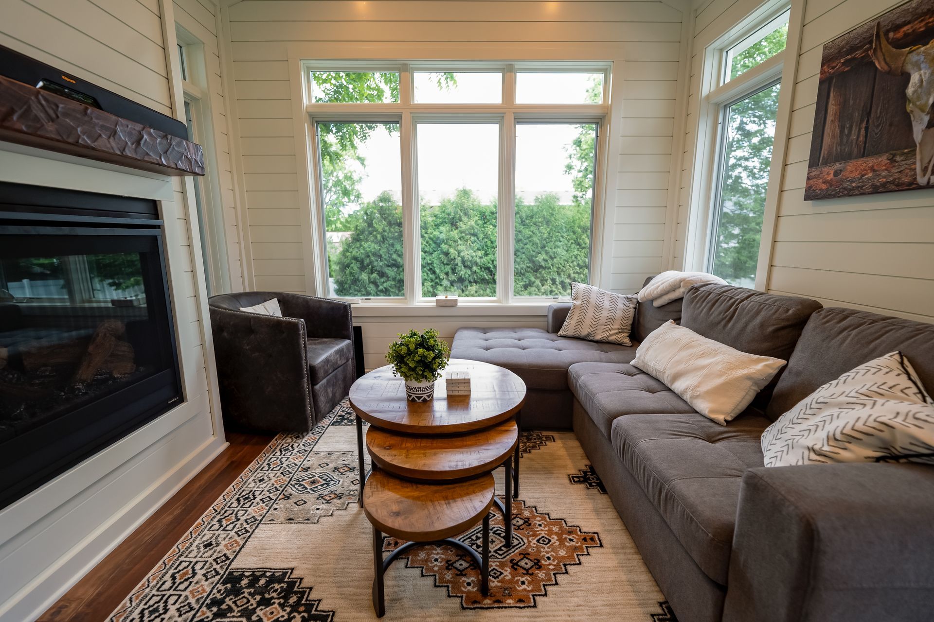Cozy living room with fireplace, gray sectional sofa, round coffee tables, and large windows with a view.