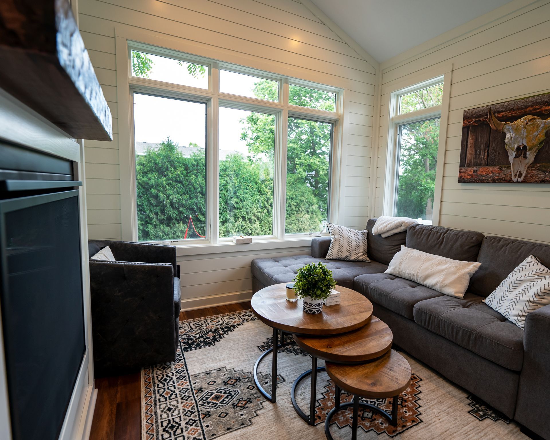 Cozy living room with a sectional sofa, coffee tables, and large windows overlooking greenery.
