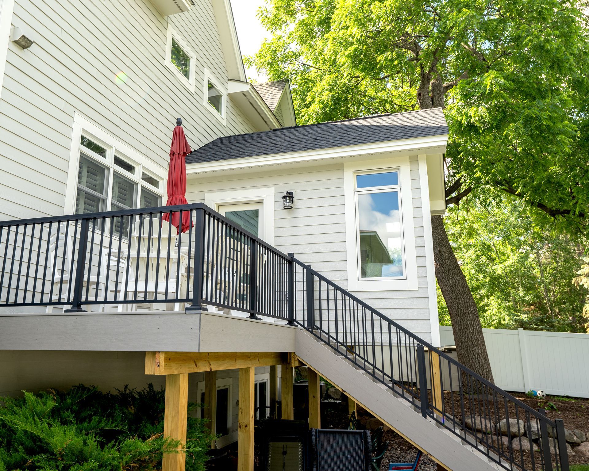 Exterior of house with deck, stairs, and small shed-like structure. Red umbrella, black railings.