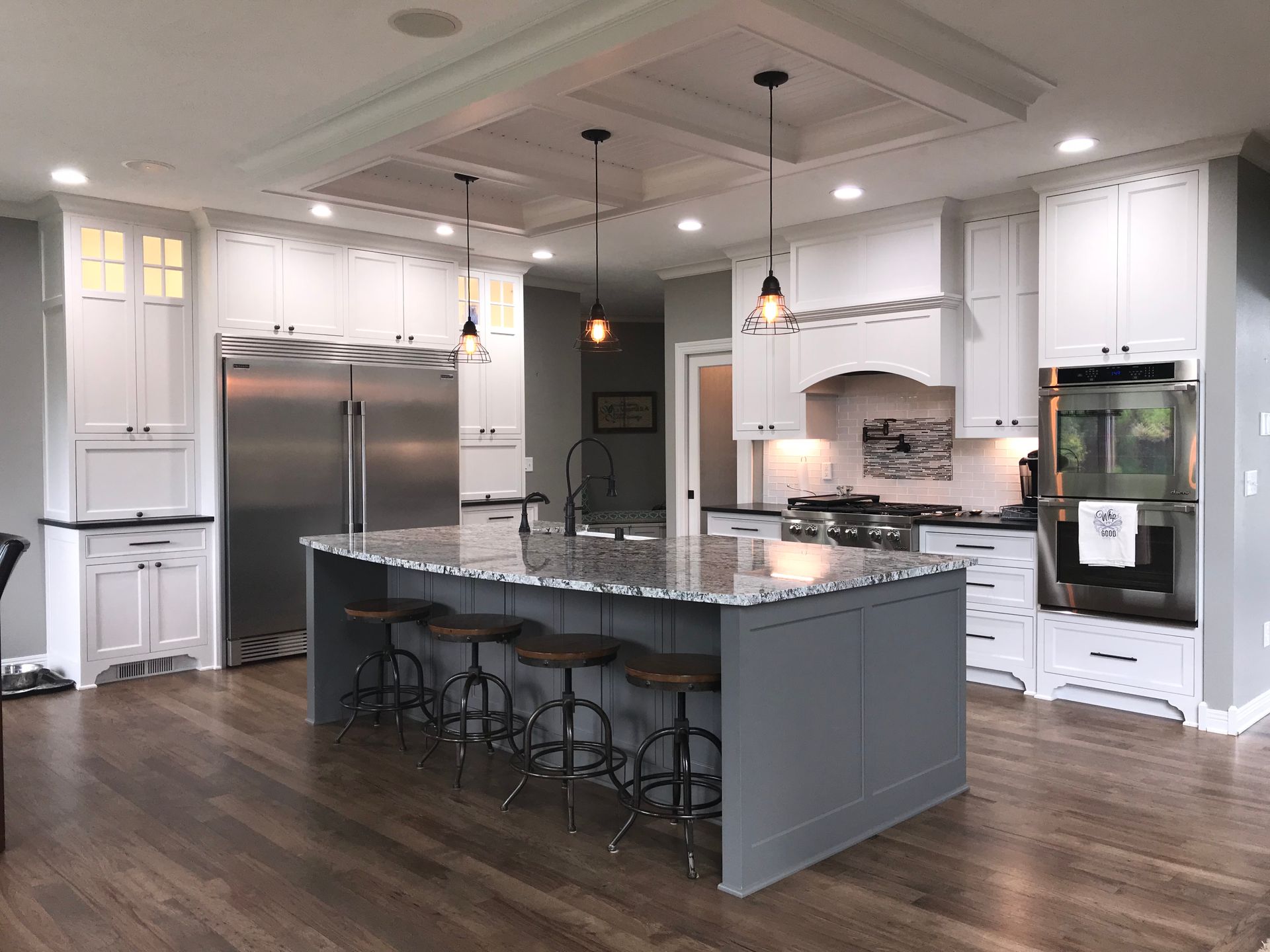 A modern kitchen with white cabinets, gray island, stainless steel appliances, and wood floor.