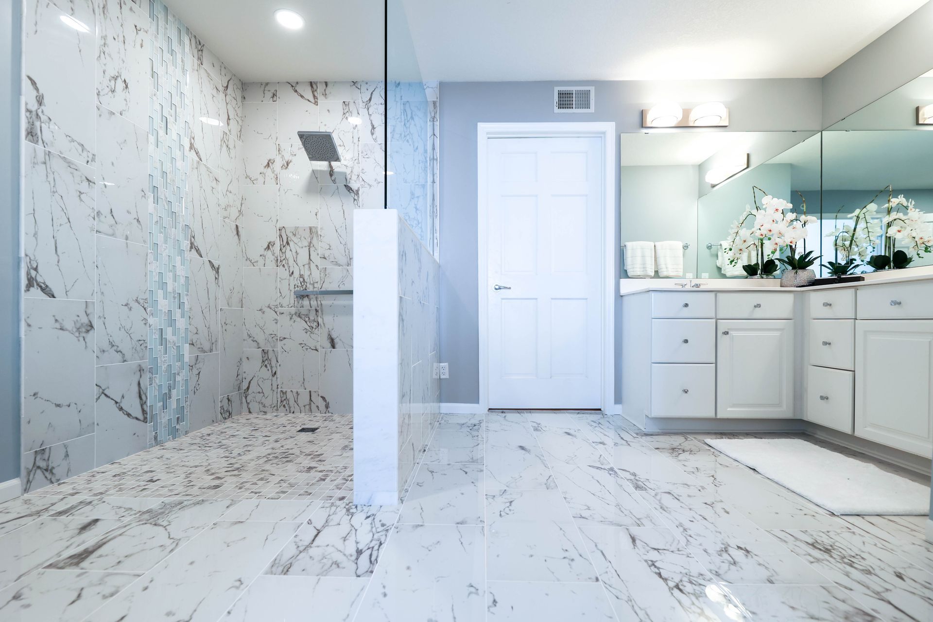Luxurious bathroom with marble walls and floors, glass shower, white vanity, and door.