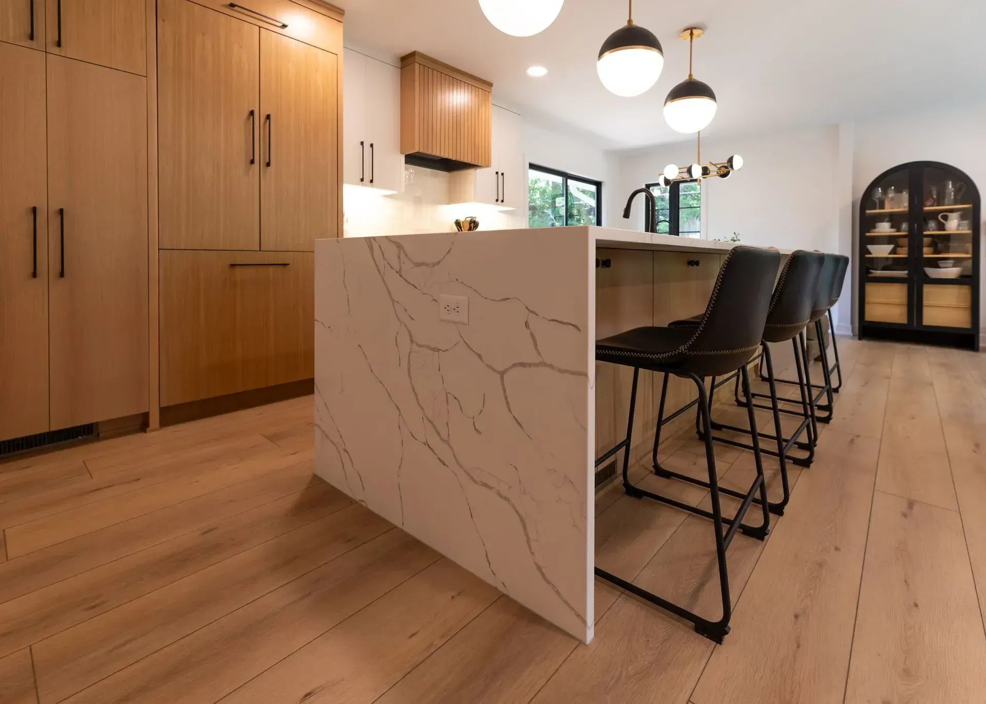 Modern kitchen with light wood cabinets, white island with black veining, and black bar stools.