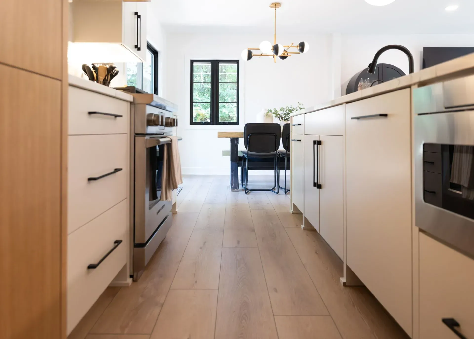 Modern kitchen with light wood floor and cabinets, stainless steel appliances, and a black window.