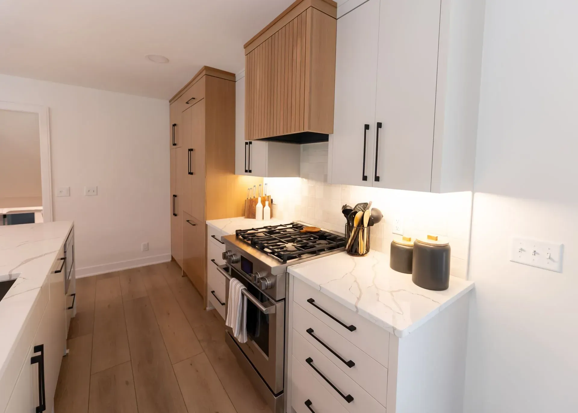 Modern white and wood kitchen with marble countertops, stainless steel appliances, and black hardware.