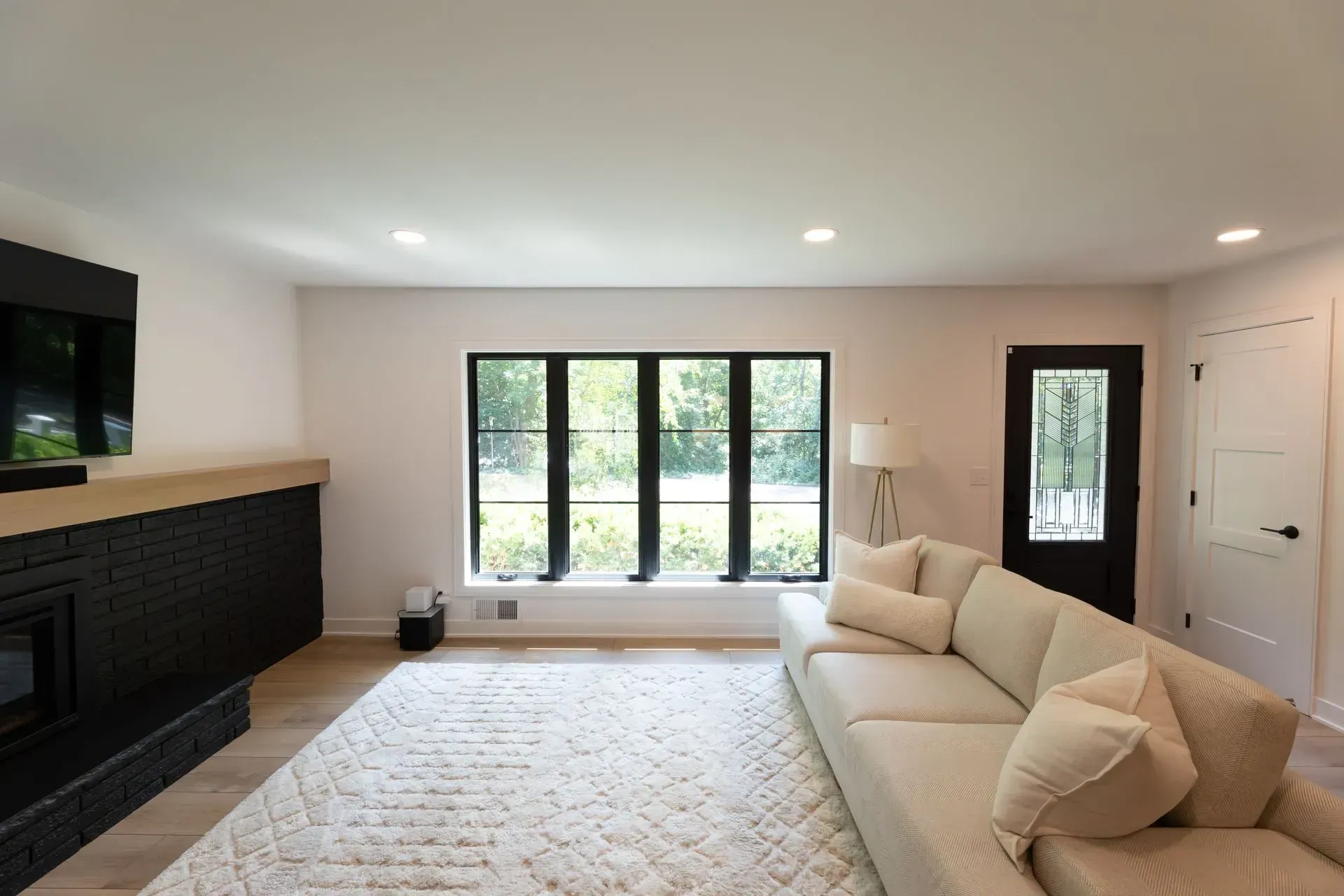 Living room with black-framed windows and fireplace, white sofa, and light wood flooring.