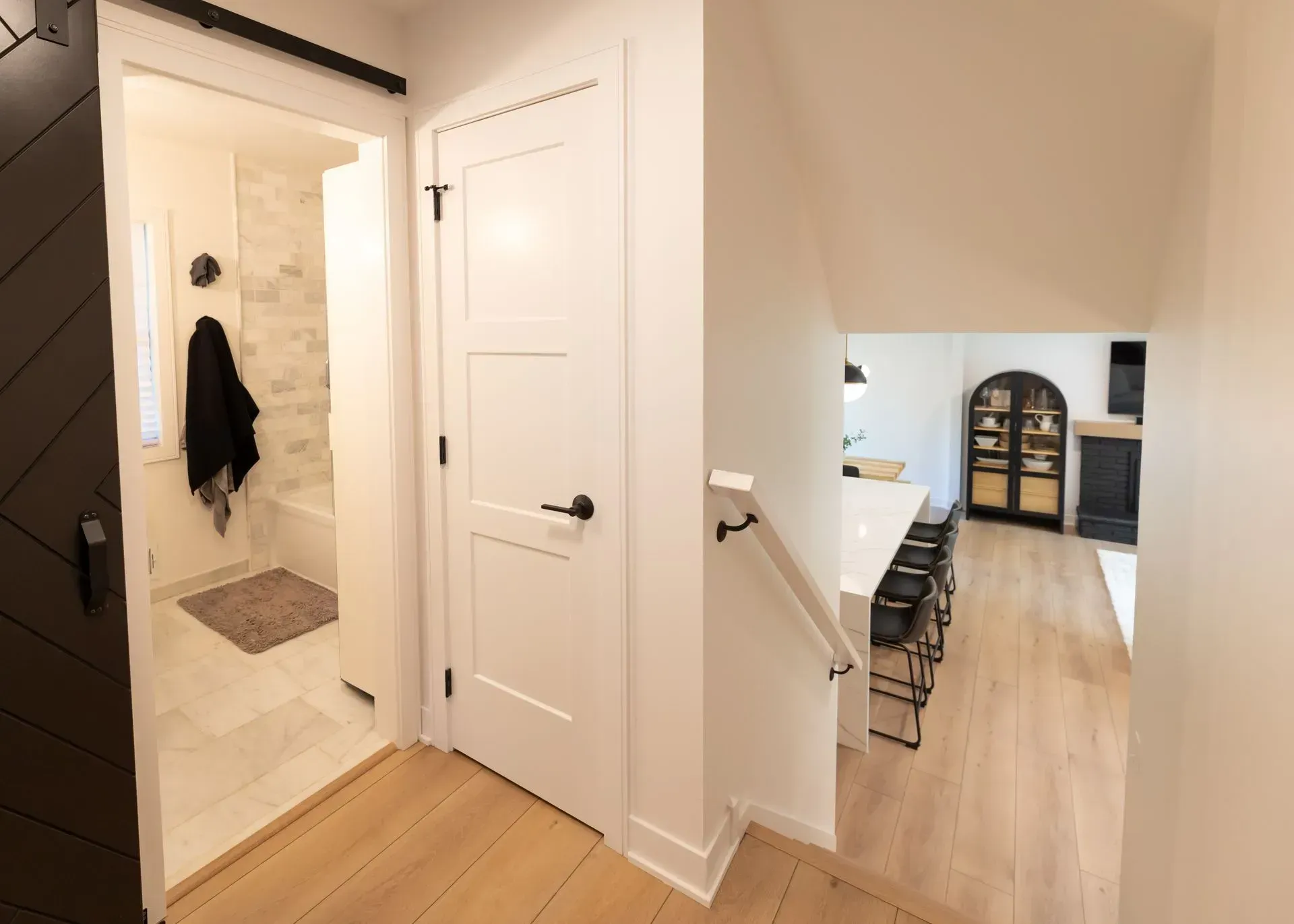 Hallway with a bathroom, stairs, and a view into a kitchen with a fireplace.