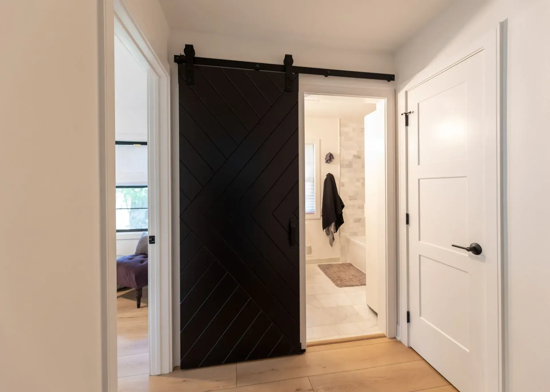 Hallway with a black sliding barn door leading to a bathroom, and a white door to a room on the right.