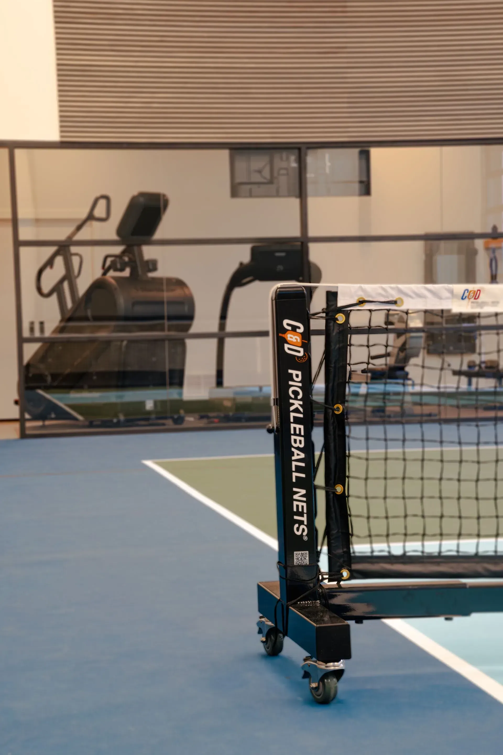 Pickleball net on a blue court, with fitness equipment visible in the background.