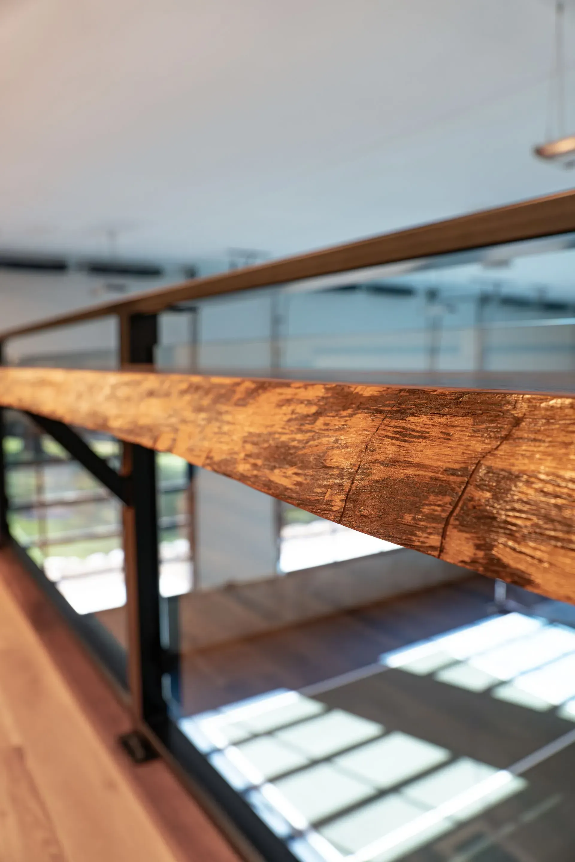 Wooden handrail with glass panels overlooking a room.