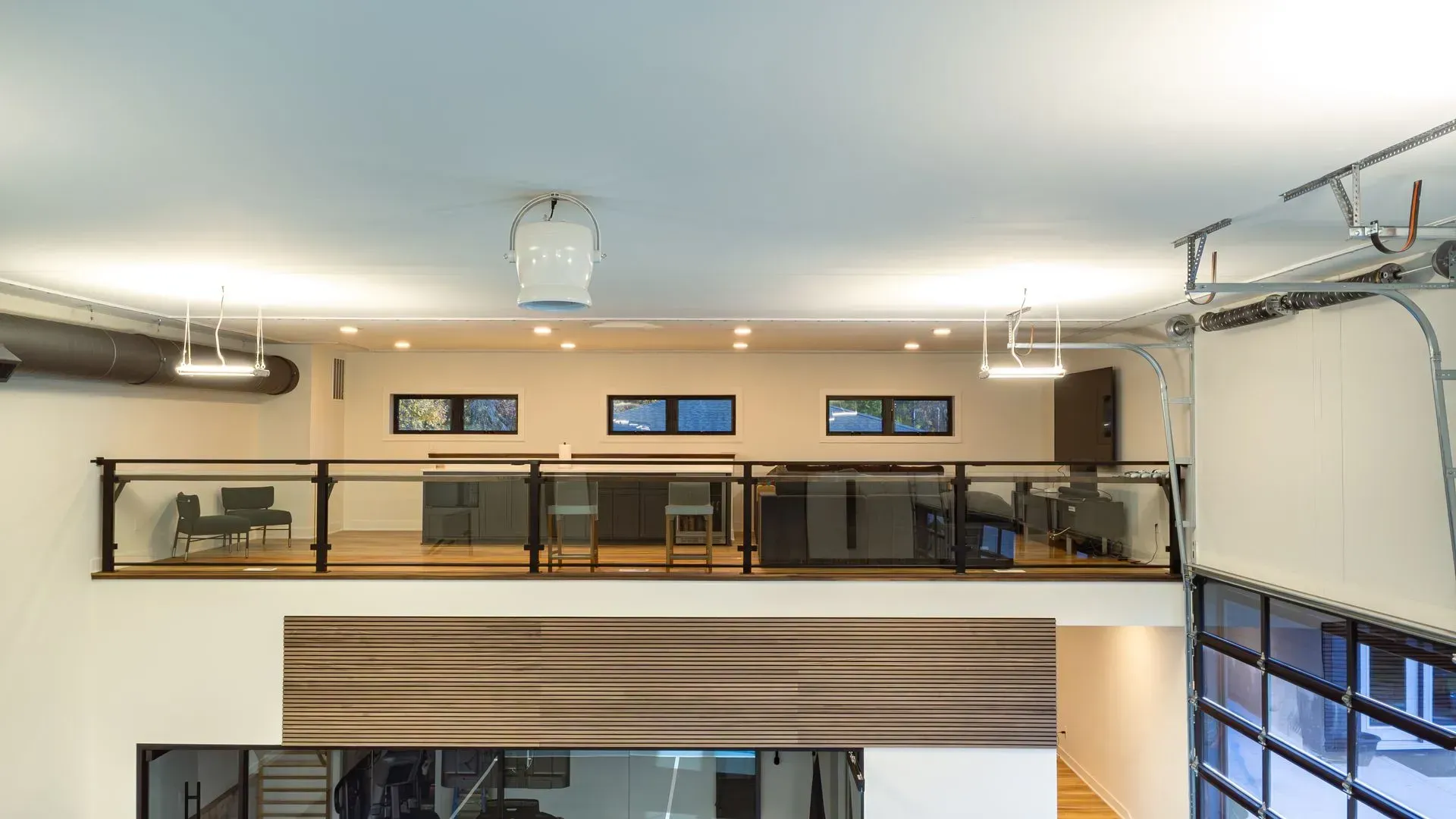 Interior view of a modern loft with a mezzanine level, glass railings, and multiple windows.