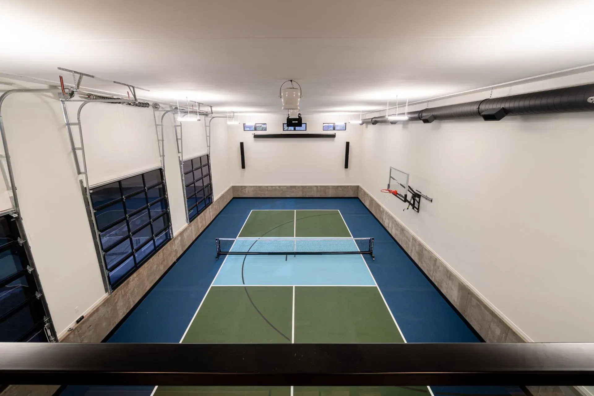 Indoor pickleball court with blue and green floor, net, and a basketball hoop.