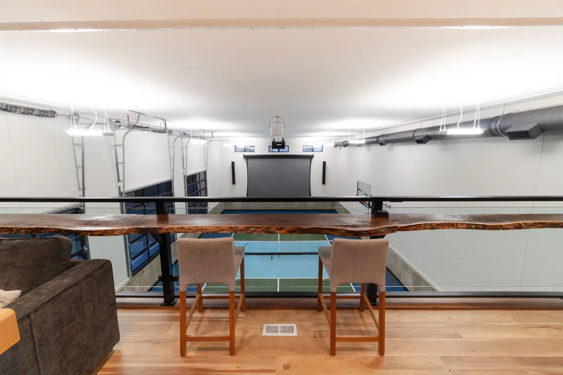 View from a balcony overlooking a sports court. Two bar stools face the court, with a long wooden bar.