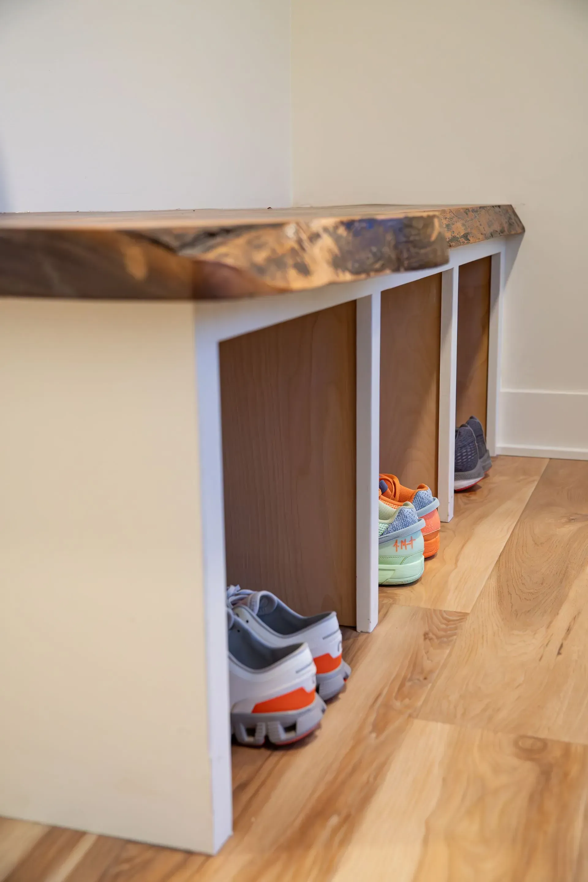 Wooden bench with shoe storage below, on a hardwood floor. White sides, natural edge top.