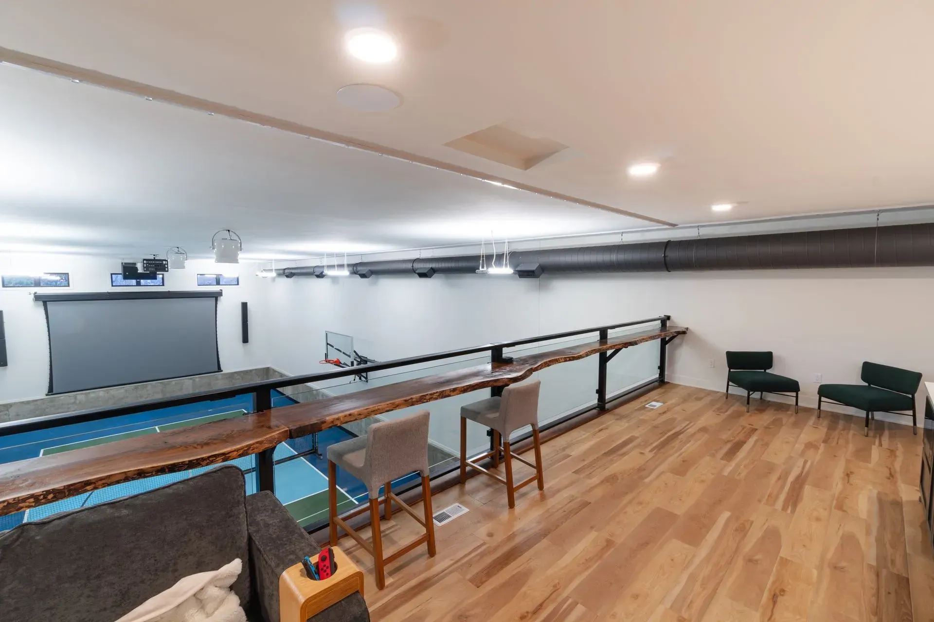 Loft with hardwood floor, bar stools, and a view of a sport court with a projection screen.