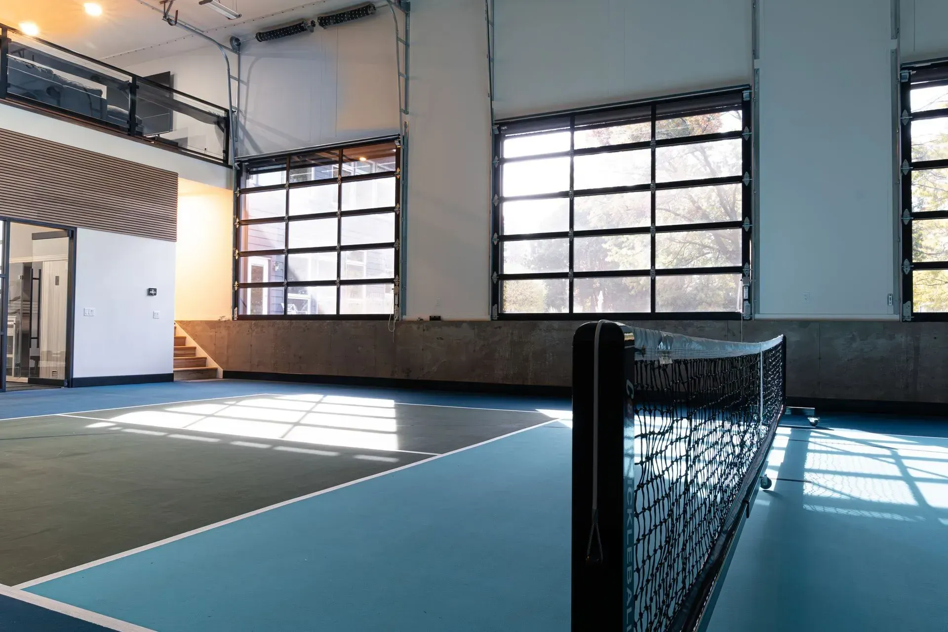 Pickleball court with a net, blue and green floor, and large windows.