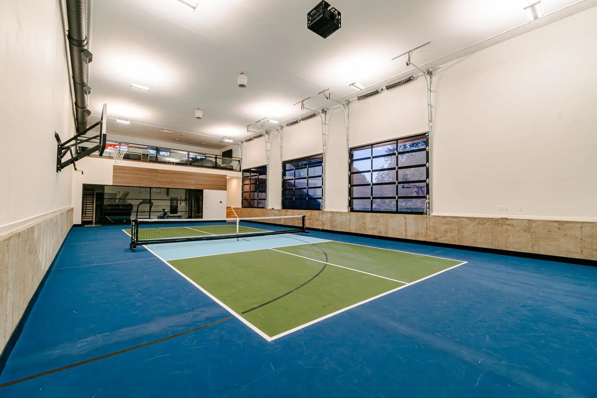 Indoor pickleball court with blue floor and green court area, net, and glass garage door windows.
