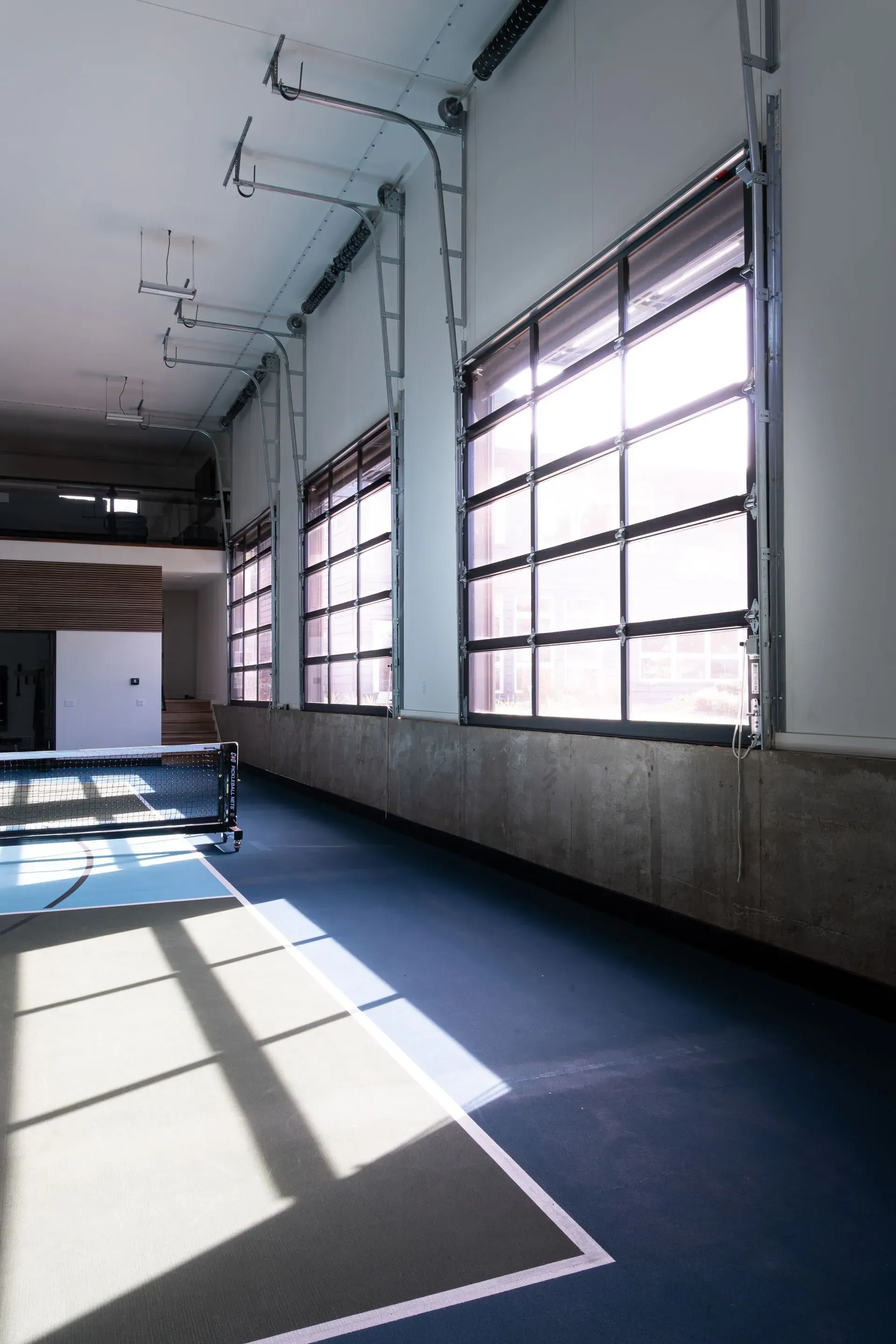 Indoor sports court with large windows; blue and grey floor; table tennis net visible.