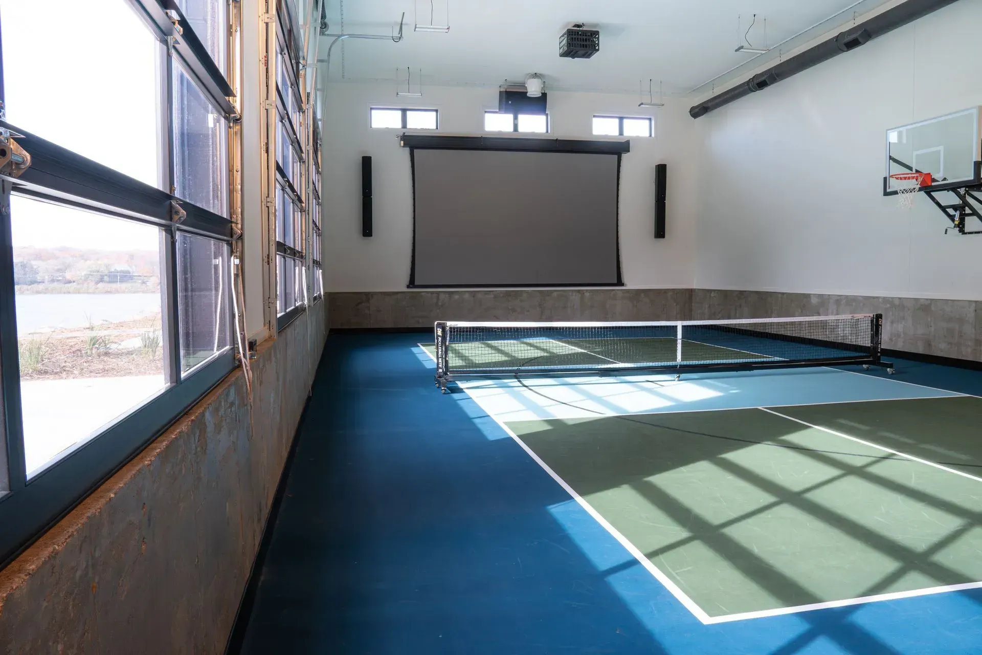 Indoor pickleball court with a retractable screen, and basketball hoop.