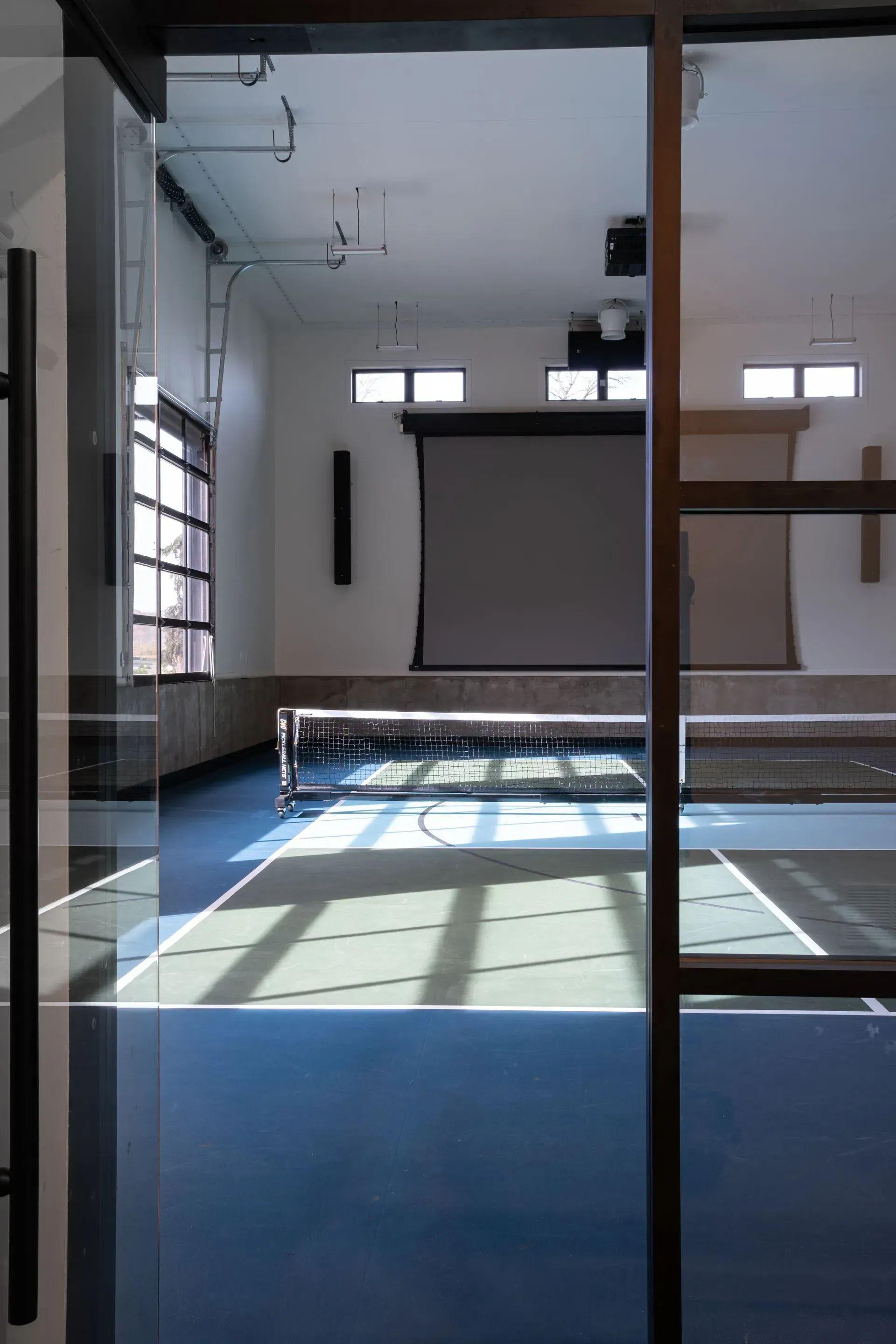 Interior view of a multipurpose room with a blue court, projector screen, and glass walls.