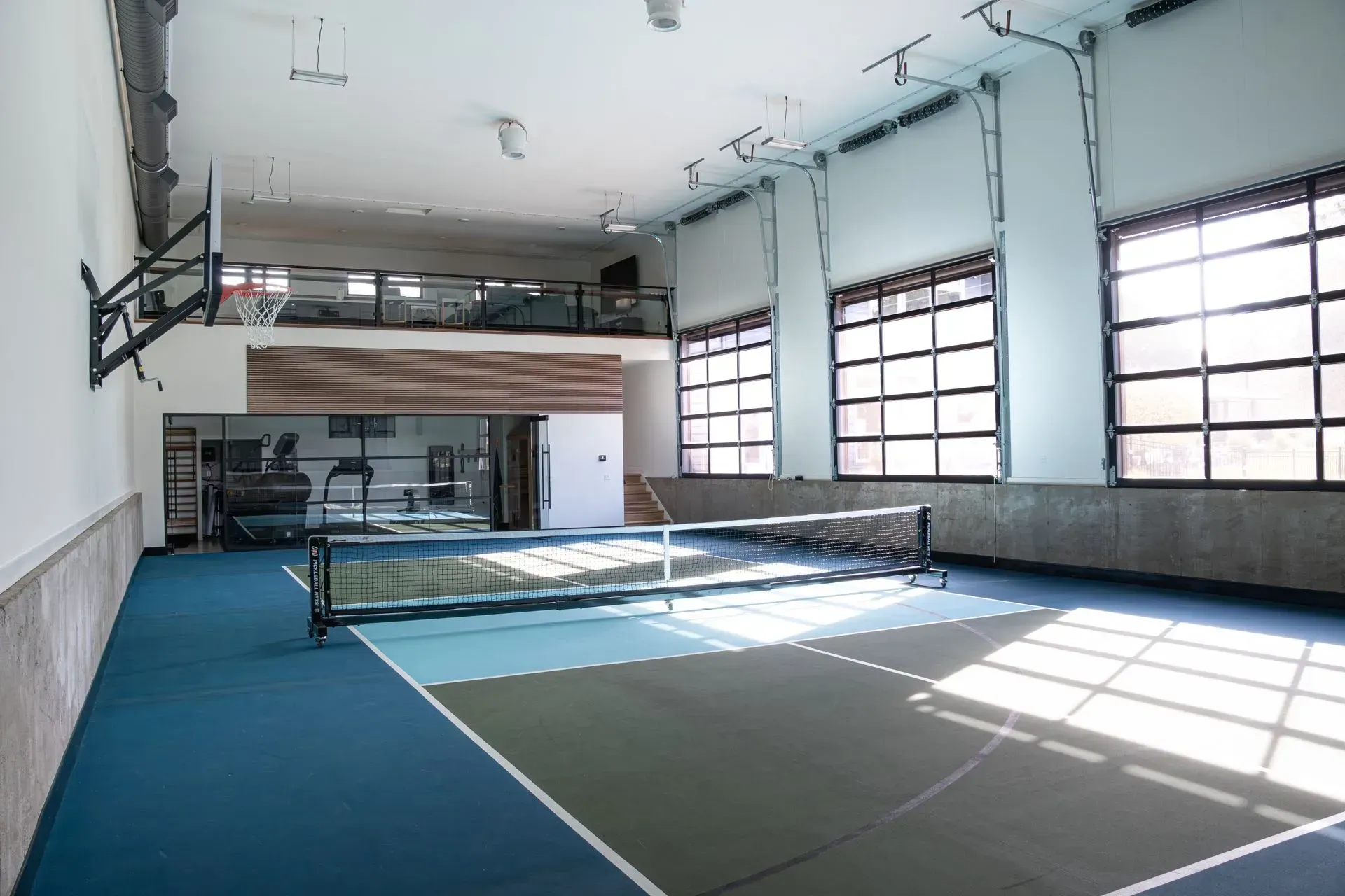 Indoor pickleball court with net, windows, mezzanine level, and fitness equipment.