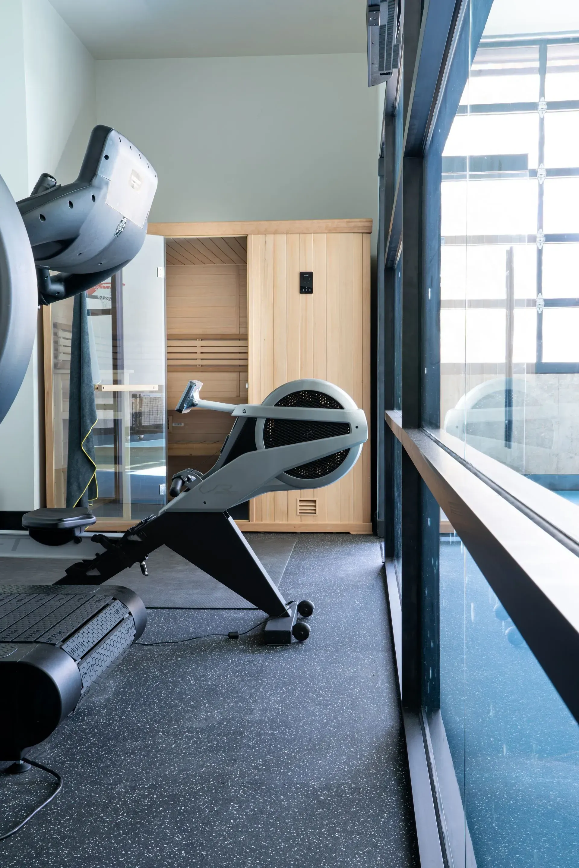 Gym interior with a rowing machine and sauna against a window.
